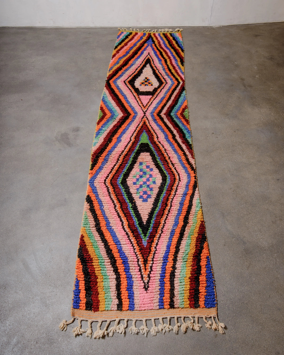 Berberlin Runner Rug made of brightly coloured wool laying flat on concrete floor.